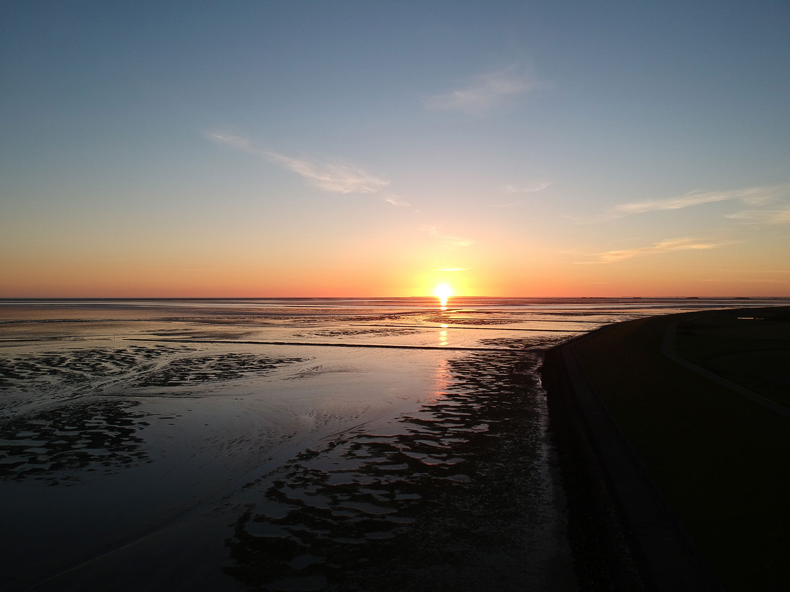 Sonnenuntergang über dem Wattenmeer der Nordsee vor der Insel Pellworm in Nordfriesland, aufgenommen vom Deich nahe der Ferienunterkunft Tammwarft 6