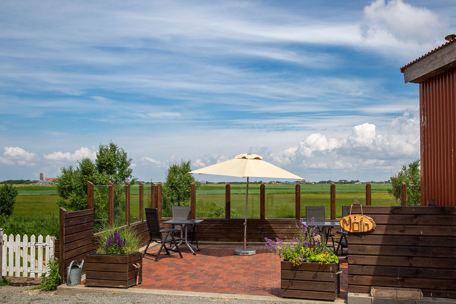 Sonnige Terrasse der Ferienwohnungen auf der Tammwarft auf Pellworm mit Sonnenschirm und Weitblick über die Marschlandschaft der Nordseeinsel