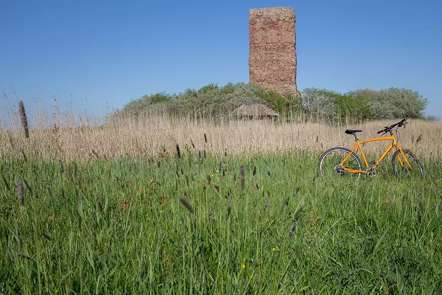 Orangefarbenes Fahrrad im Gras vor dem historischen Fething-Turm der Tammwarft auf Pellworm – Radtour entlang der offiziellen Fahrradroute in Nordfriesland